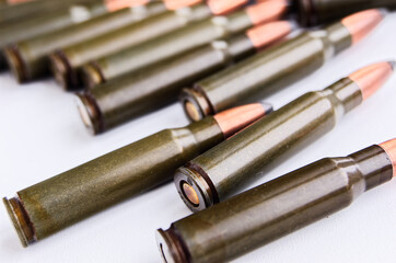 Green-coated rifle ammunition lay diagonally on white surface, bullets tips, brass casings, and...
