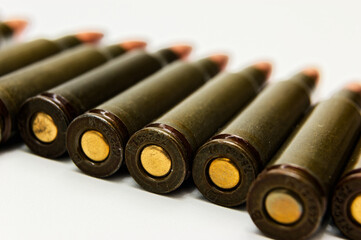 Rifle ammunition cartridges line up neatly against plain white background. Dark green casings with...