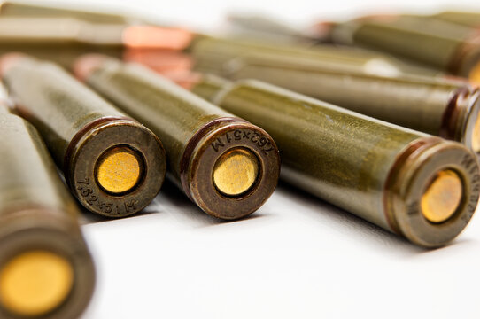 Several M193 5.56x45mm NATO rifle cartridges lay diagonally on white background, showcasing olive drab bodies and brass-colored tips. Textured metal surfaces and headstamps are emphasized, making this