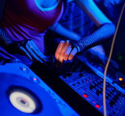 DJ performs at nightclub illuminated by blue mood lighting, focusing on mixing tracks with...