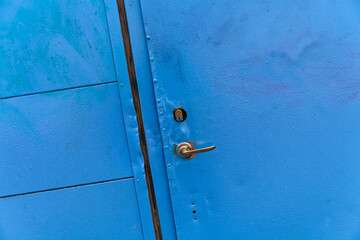 Vintage blue metal door stands weathered with a brass knob and keyhole peeking through rust and chipping paint. Highlights include an aged patina and visible lock mechanism, perfect for industrial or