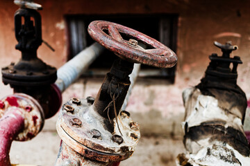 Abandoned stained pipes valve corrode and crack in an old, neglected factory. Rusty valves, flanges, and stained concrete surround brick walls with graffiti and closed metal door.