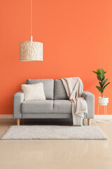 Comfortable beige sofa and houseplant near orange wall in interior of living room