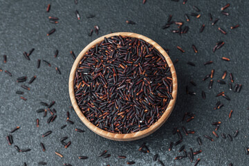 Black rice in wooden bowl surrounded by scattered grains