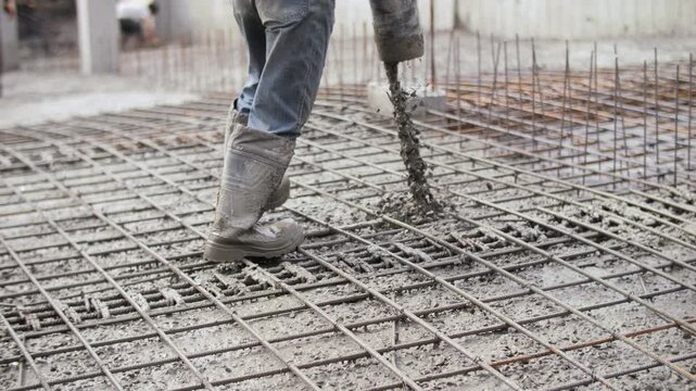 Worker pouring and vibrating concrete on reinforcement at construction site
