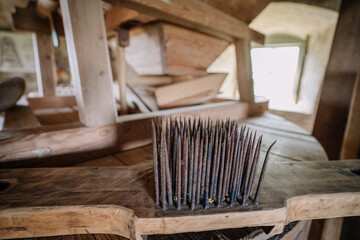 Close-up of a vintage wool carding tool with sharp metal spikes used in traditional textile processing, placed inside a rustic wooden interior.
