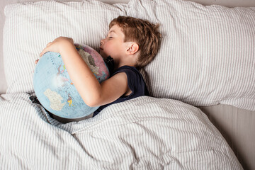 Peaceful boy sleeping with globe in bed, representing childhood dreams, imagination, innocence, hope for the future, and the vision of a better connected world full of possibilities.
