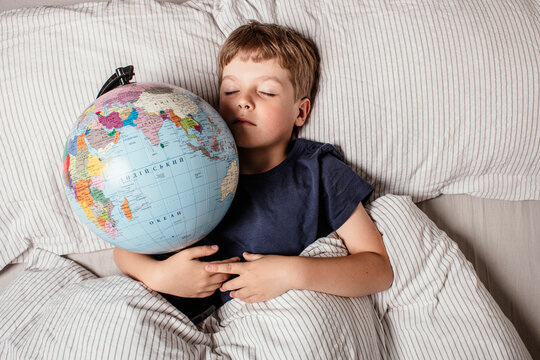 Peaceful boy sleeping with globe in bed, representing childhood dreams, imagination, innocence, hope for the future, and the vision of a better connected world full of possibilities.