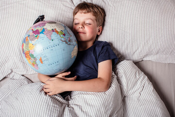 Boy sleeping in bed with globe, dreaming of travel, adventure, exploring new countries and cultures, symbolizing wanderlust, future journeys, and the dream of discovering the world.
