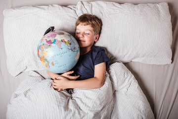 Boy sleeping in bed with globe, dreaming of travel, adventure, exploring new countries and cultures, symbolizing wanderlust, future journeys, and the dream of discovering the world.
