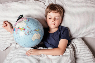 Boy sleeping in bed with globe, dreaming of travel, adventure, exploring new countries and cultures, symbolizing wanderlust, future journeys, and the dream of discovering the world.
