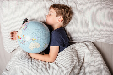 Child resting in bed with a globe, symbolizing learning, geography, global education, curiosity, and the importance of knowledge for the younger generation in a connected world.
