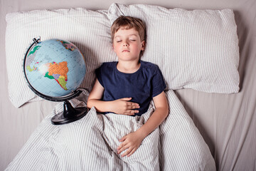 Child resting in bed with a globe, symbolizing learning, geography, global education, curiosity, and the importance of knowledge for the younger generation in a connected world.
