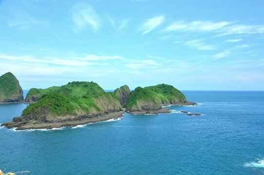 A beautiful coastal landscape at Bedil Island, Banyuwangi, Indonesia. Lush green hills covered in dense vegetation rise dramatically from the clear blue ocean
