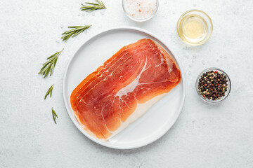 Prosciutto slices on white plate with rosemary and salt