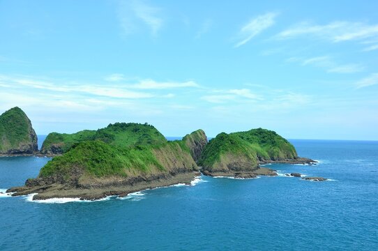 A beautiful coastal landscape at Bedil Island, Banyuwangi, Indonesia. Lush green hills covered in dense vegetation rise dramatically from the clear blue ocean