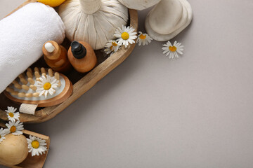 Wooden tray, towel, bottles of cosmetic product and chamomile flowers on grey background, closeup