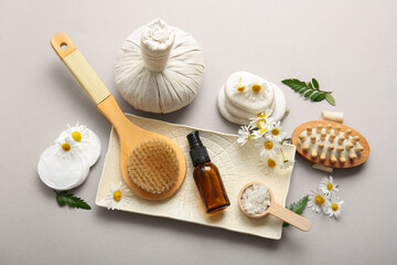 Fototapeta na wymiar Composition with massage body brushes, bottles of cosmetic products and chamomile flowers on grey background, closeup