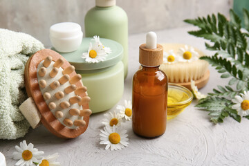 Chamomile flowers, massage body brush, bottle and jars of cosmetic products on grey grunge background, closeup