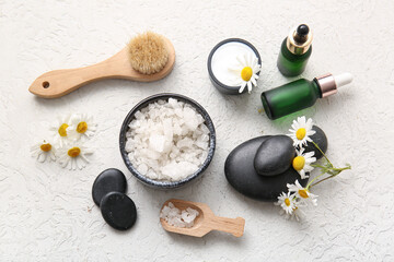 Chamomile flowers, spa stones and bottles of cosmetic products on grey grunge background, closeup