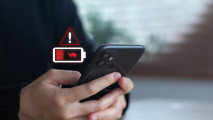 Close-up hand holding a smartphone with a low battery warning icon. Concept of mobile power alert, smartphone charging, energy crisis, battery problem, digital device usage, and technology lifestyle.
