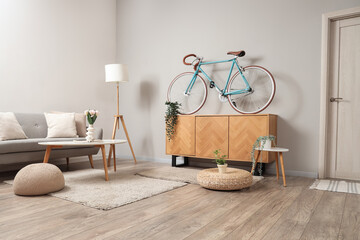 Interior of light living room with bicycle, commode and sofa
