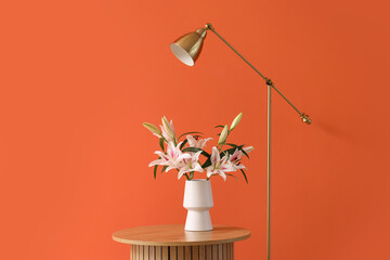 Stylish wooden coffee table with bouquet of flowers and standard lamp near orange wall