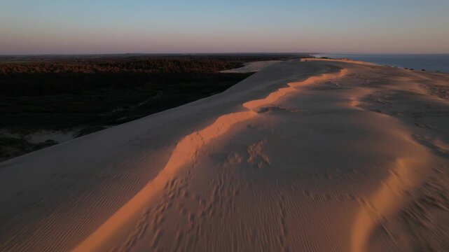 Aerial top view of dramatic coastal sand cliffs and shoreline at sunset. Natural erosion patterns with orange evening light reflecting on the beach and sea in Northern Denmark
