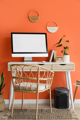 Comfortable workspace with modern computer, anthurium flower and calendar near orange wall