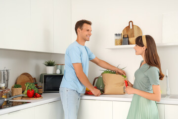 Young couple with paper bag of food on counter in kitchen