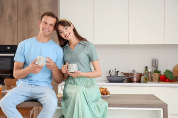 Young couple with cups of coffee sitting on table in kitchen