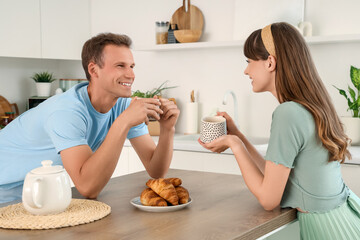 Young couple with cups of tea and croissants at table in kitchen