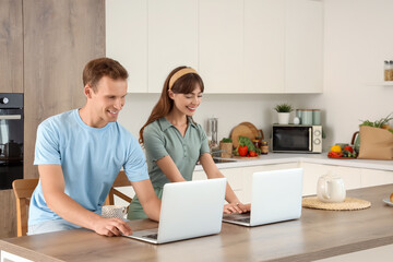 Young couple using laptops in kitchen