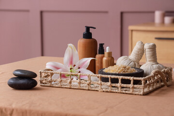 Wicker tray with cosmetic products, spa accessories and lily flower on table