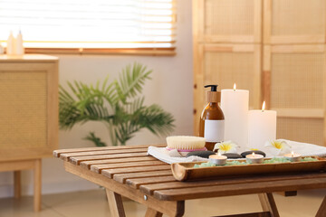 Composition with spa accessories, bottle of cosmetic product and burning candles on wooden table in salon