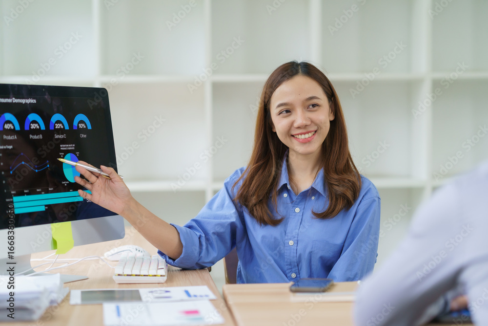 Poster asian businesswoman explaining charts and graphs on a computer screen to a colleague during a busine