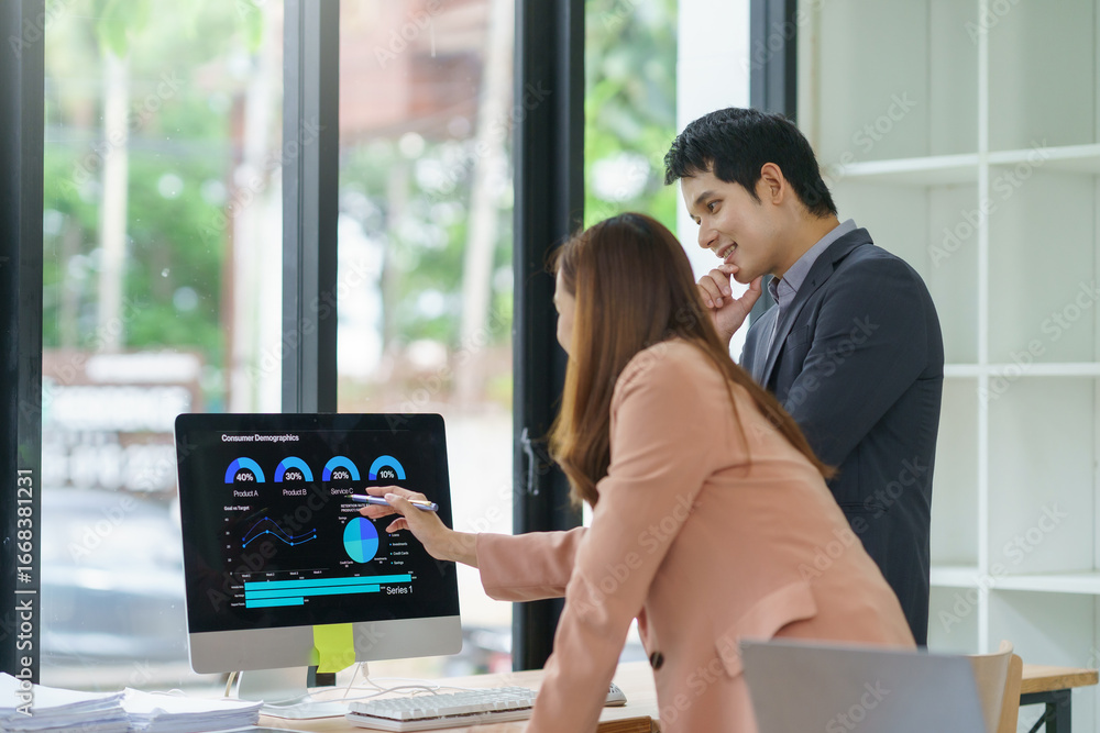 Poster businesswoman pointing at computer screen showing charts and graphs while discussing with businessma