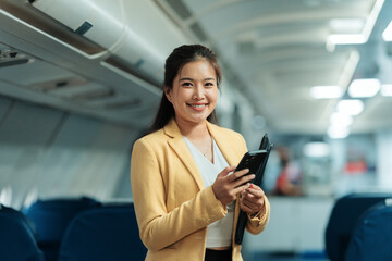 Asian businesswoman holding a folder and using a mobile phone while seated in an airplane cabin, enjoying her travel experience