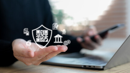 Hand showing a hologram QR code with a shield security icon. Concept of secure payment, digital banking, fintech, online transaction, cyber protection, e-commerce, and financial technology innovation.