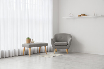 Interior of living room with light curtain, grey armchair and soft bench