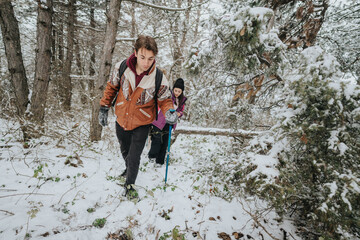 Two young friends wearing jackets traverse a snowy woodland terrain, enjoying the beauty and...