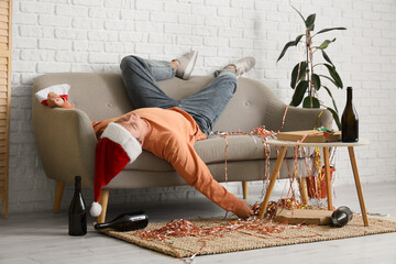 Drunk young man in Santa hat sleeping on sofa at home after Christmas party