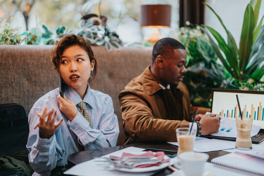 Two business people collaborating on ideas in a modern setting. One is engaged on a call while another reviews data on a laptop. The scene emphasizes teamwork, strategy, and productivity.