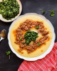 Angu with bolognese sauce and braised taioba on a white plate on a black background, typical Brazilian food from Minas Gerais