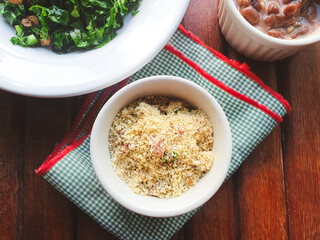Farofa with bacon in a white porcelain bowl, typical Brazilian food, on a wooden background
