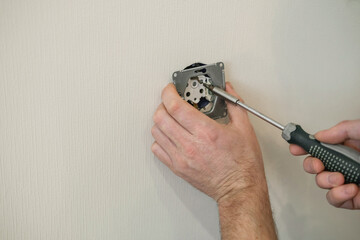 Close-up of hands screwing socket with a screwdriver against light wall. Home renovation,...