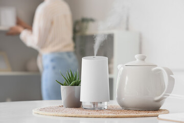 Air humidifier with plant and teapot on dining table in room, closeup