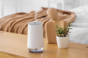 Air humidifier with plant and statuette on bench in bedroom, closeup