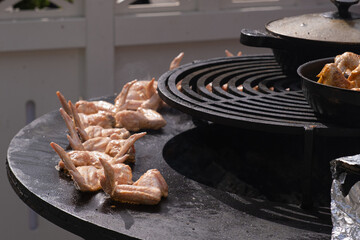 Close-up of raw chicken wings placed on a hot circular grill over open fire, prepared for cooking...