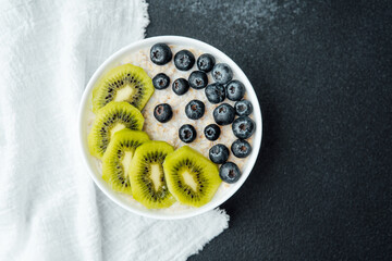 Healthy breakfast bowl with kiwi slices and blueberries on dark background